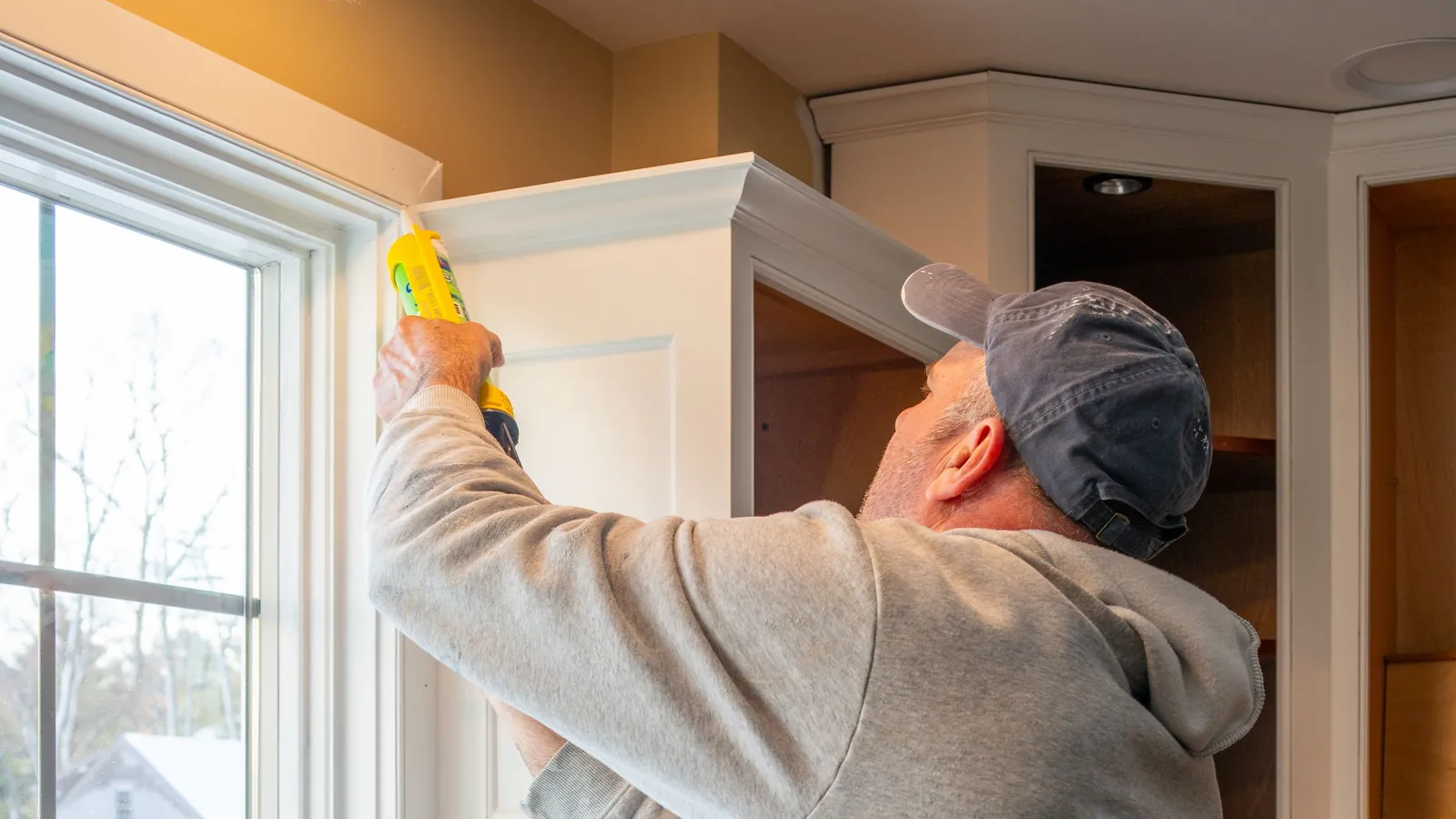 Carpenter caulking new kitchen cabinets during a home renovation