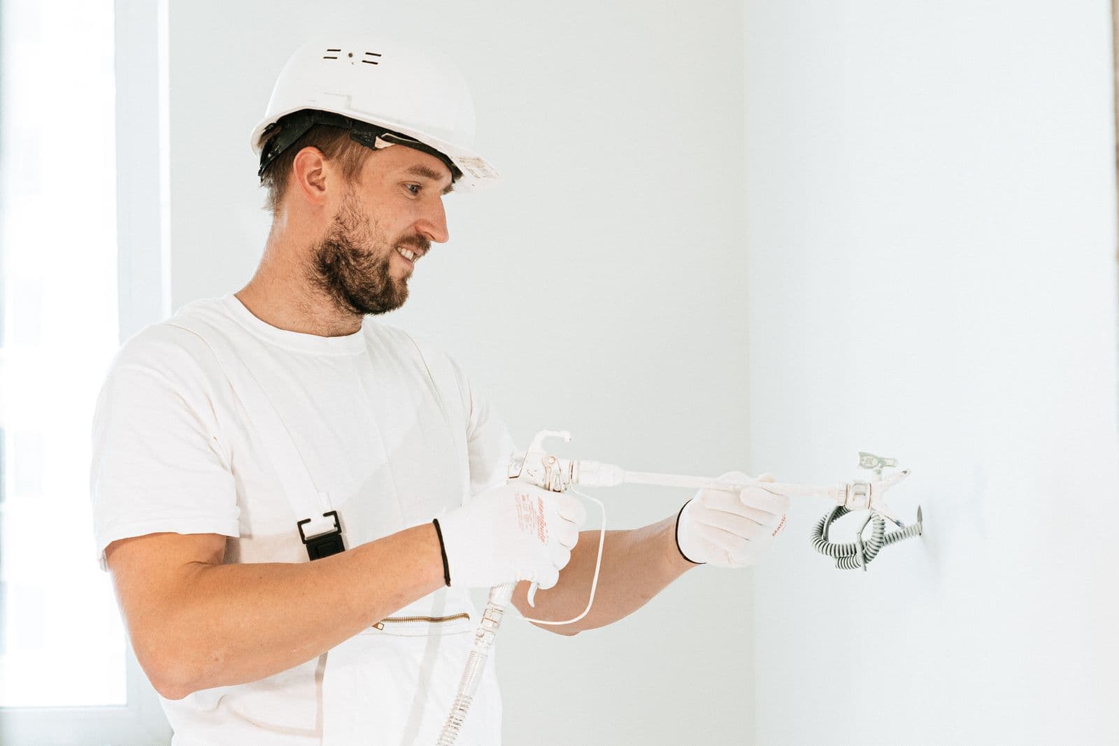 A tradesperson in white work clothes finishing an interior wall with a spray tool