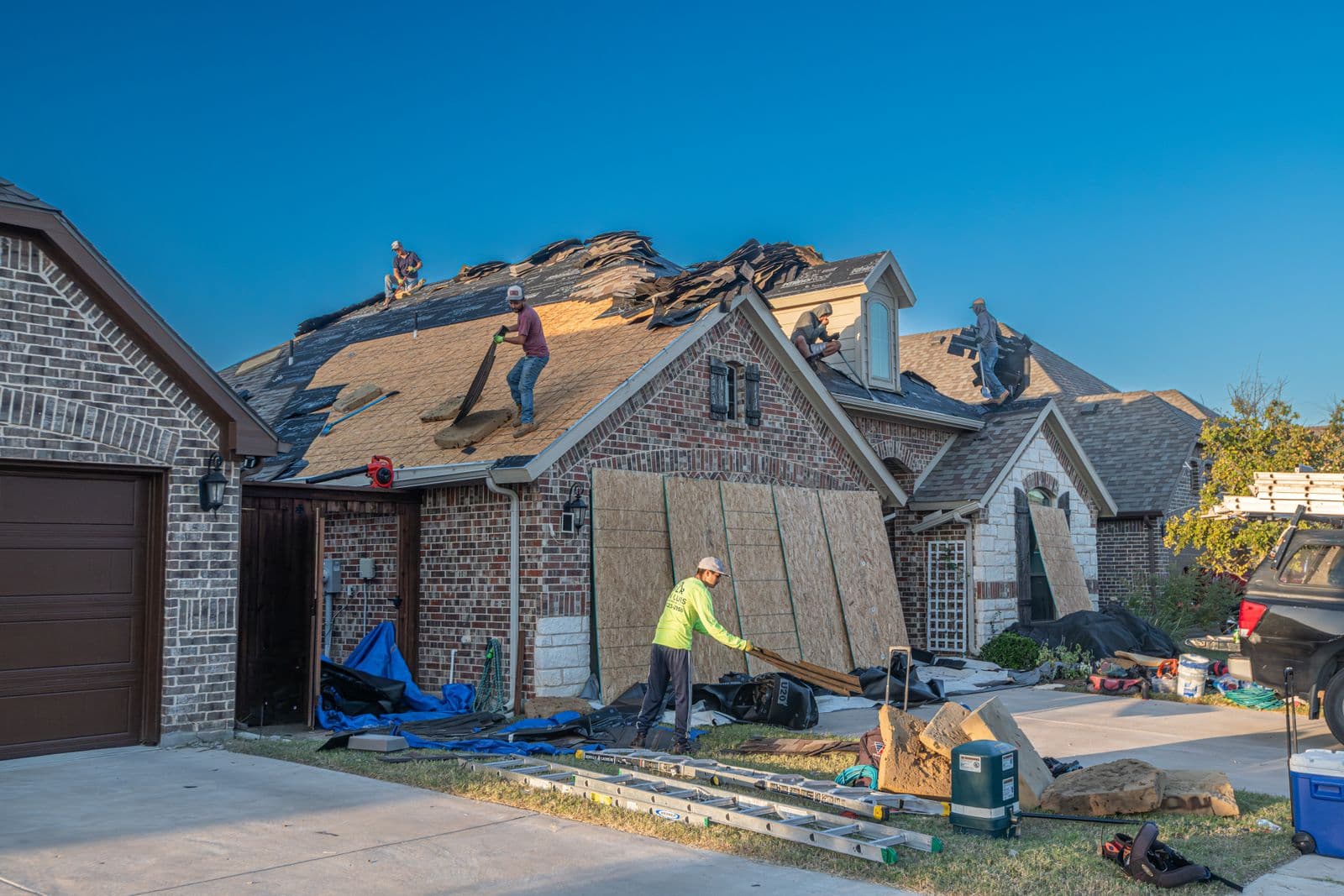 A roofing crew tearing off and replacing the roof covering on a two-storey brick house