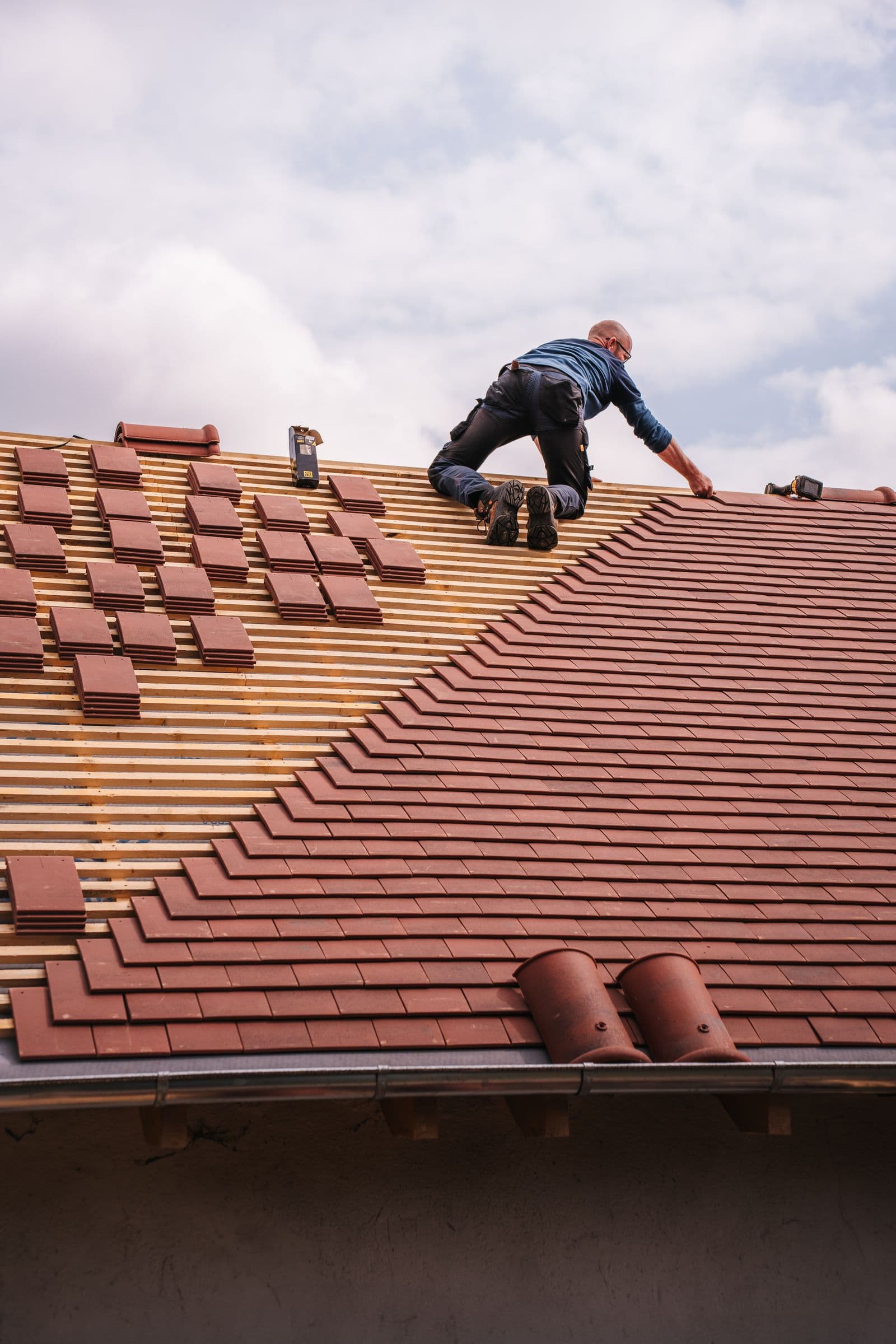 A roofer installing interlocking tile roof covering over battens on a residential roof