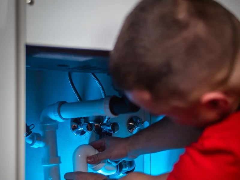 Technician fitting pipework inside a sink cabinet for point-of-use treatment