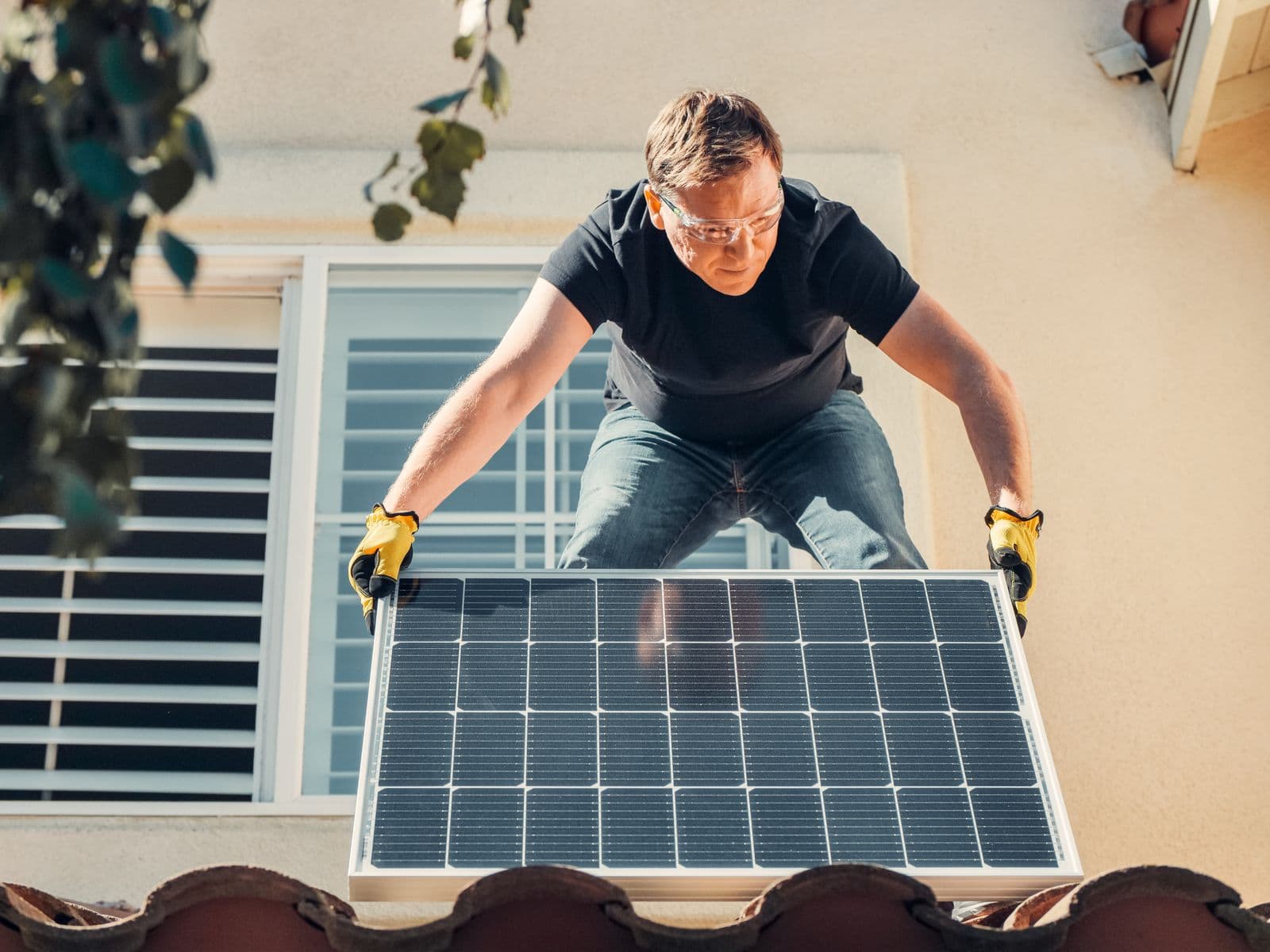 An installer lowering a solar panel into place on a tiled roof, seen from above