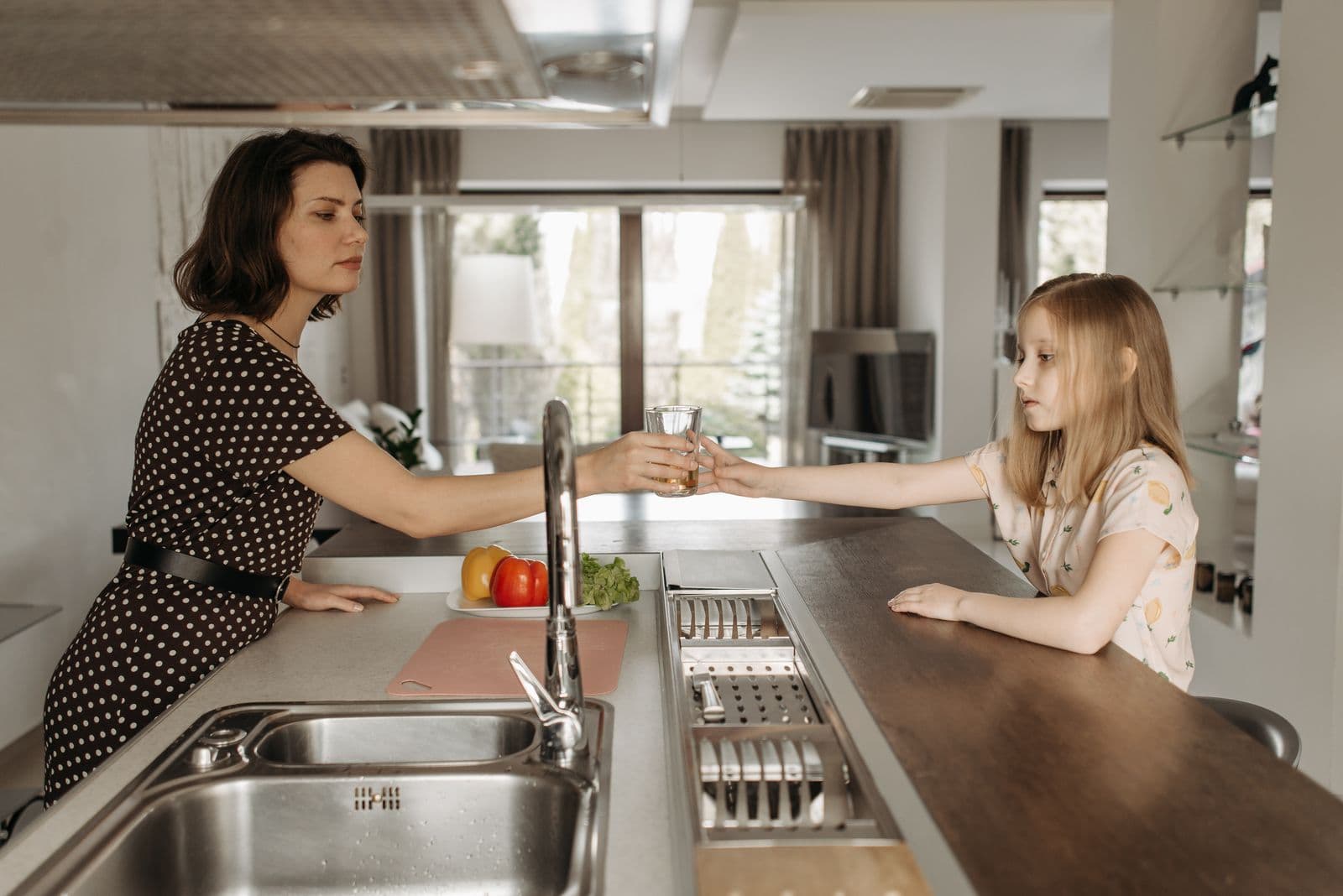 An adult handing a glass of water to a child across a kitchen counter