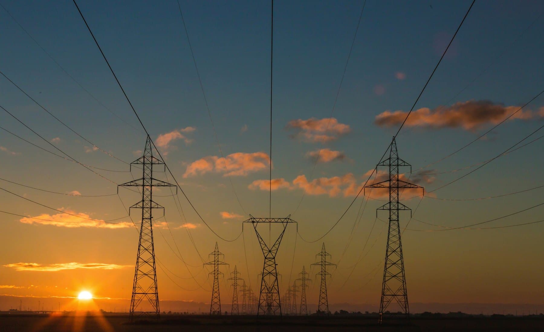 High-voltage transmission lines at sunset — the grid a home battery is independent of during an outage