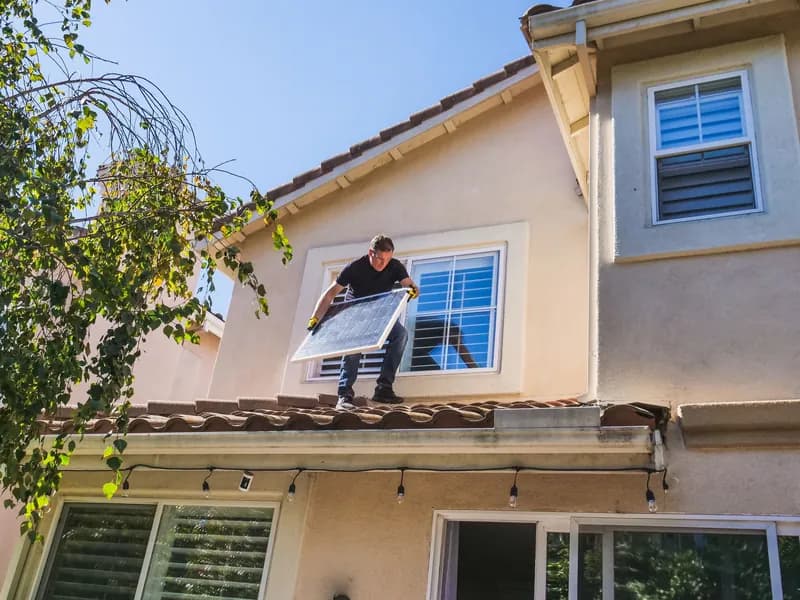 Installer carrying a solar panel across the tile roof of a two-story home