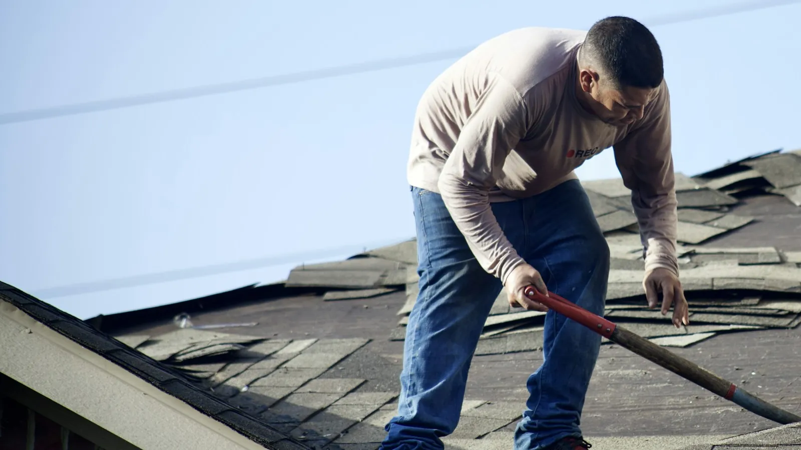 Roofer tearing off old asphalt shingles on a home roof