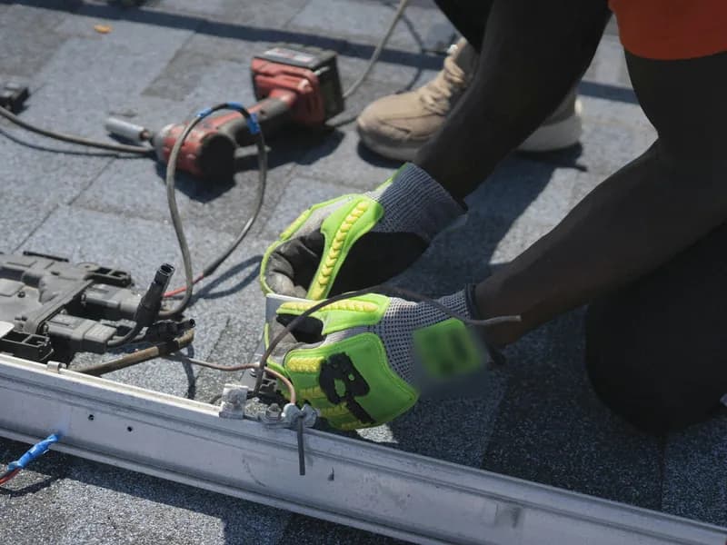 Installer wiring components on a mounting rail on a shingled roof