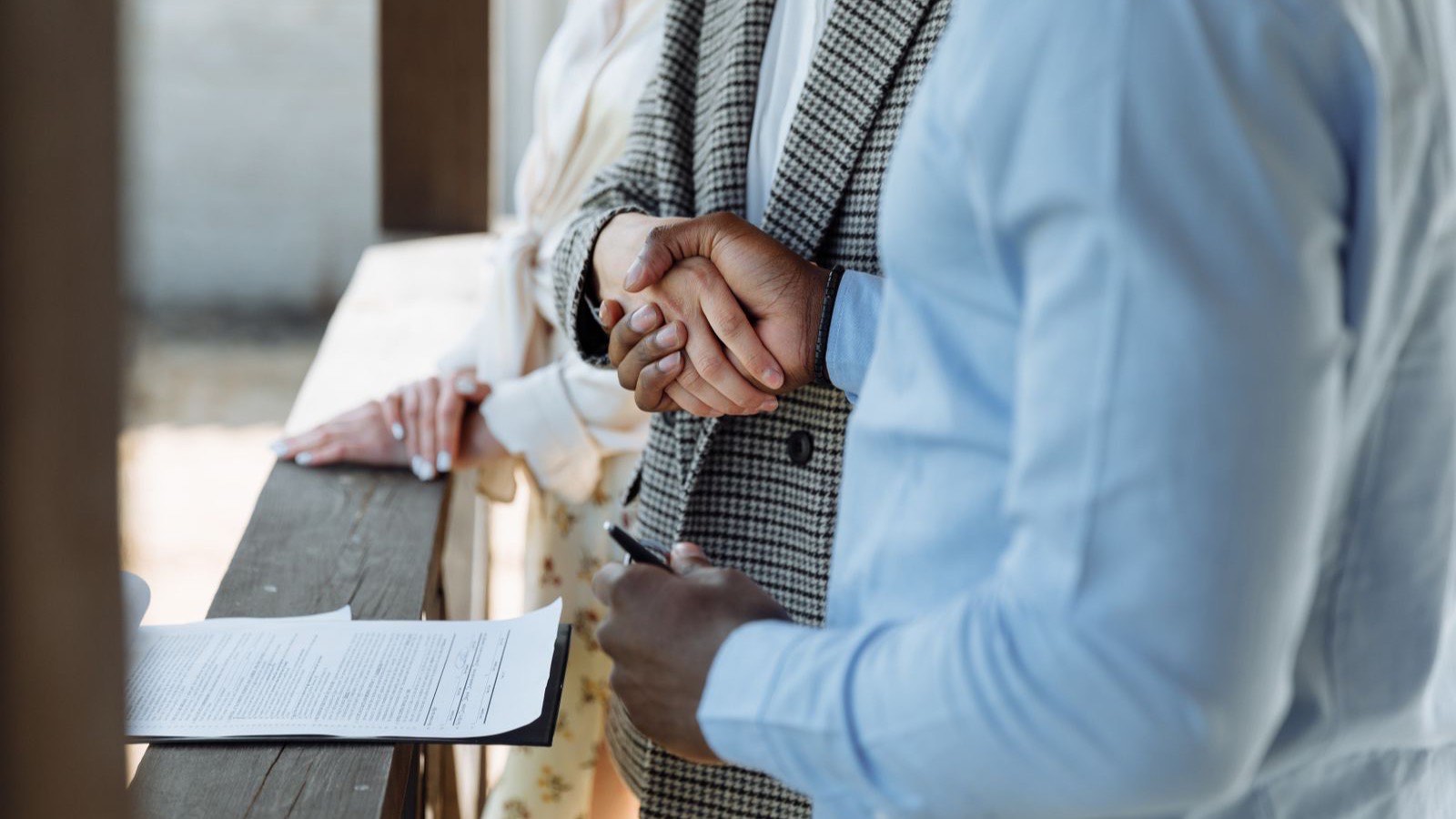 Two people shaking hands beside a signed multi-page agreement resting on a wooden ledge, with a pen still in hand